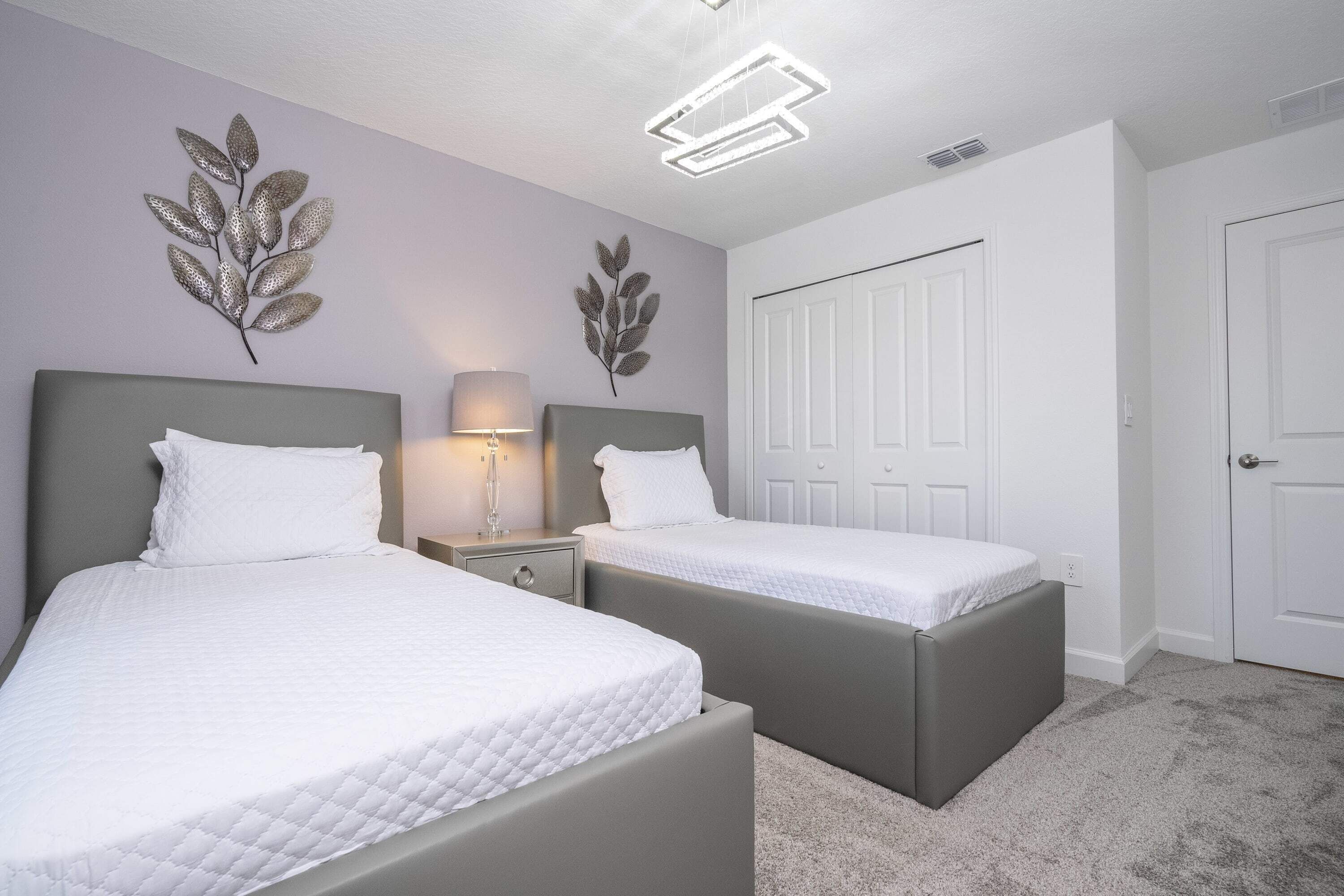 A bedroom with two beds, a nightstand, a lamp, and decorative leaf wall art.