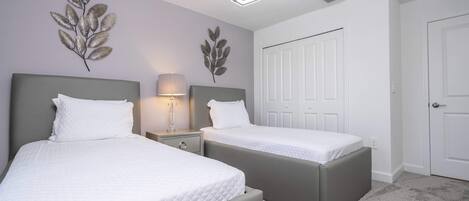 A bedroom with two beds, a nightstand, a lamp, and decorative leaf wall art.