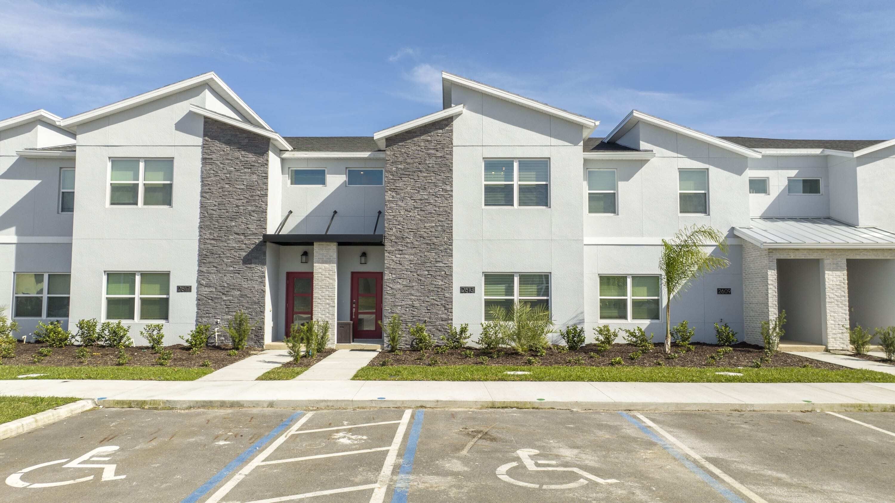 A modern apartment building with a central entrance, multiple windows, and a parking area with handicapped accessibility.