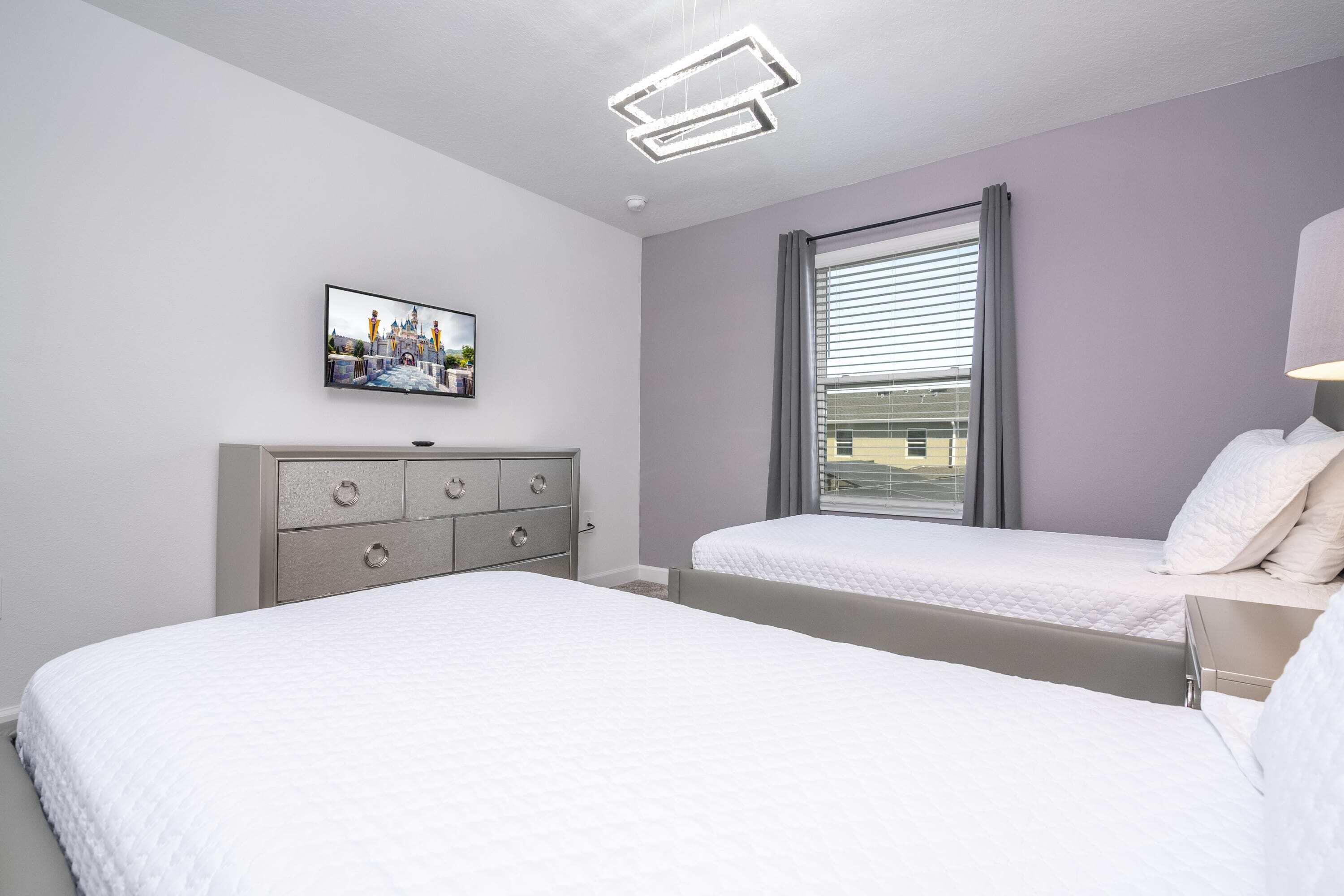 Een moderne hotelkamer met twee bedden, een dressoir, een flatscreen televisie en een raam met luxaflex.