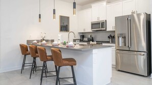 A modern kitchen with white cabinets, stainless steel appliances, and a central island with bar stools.