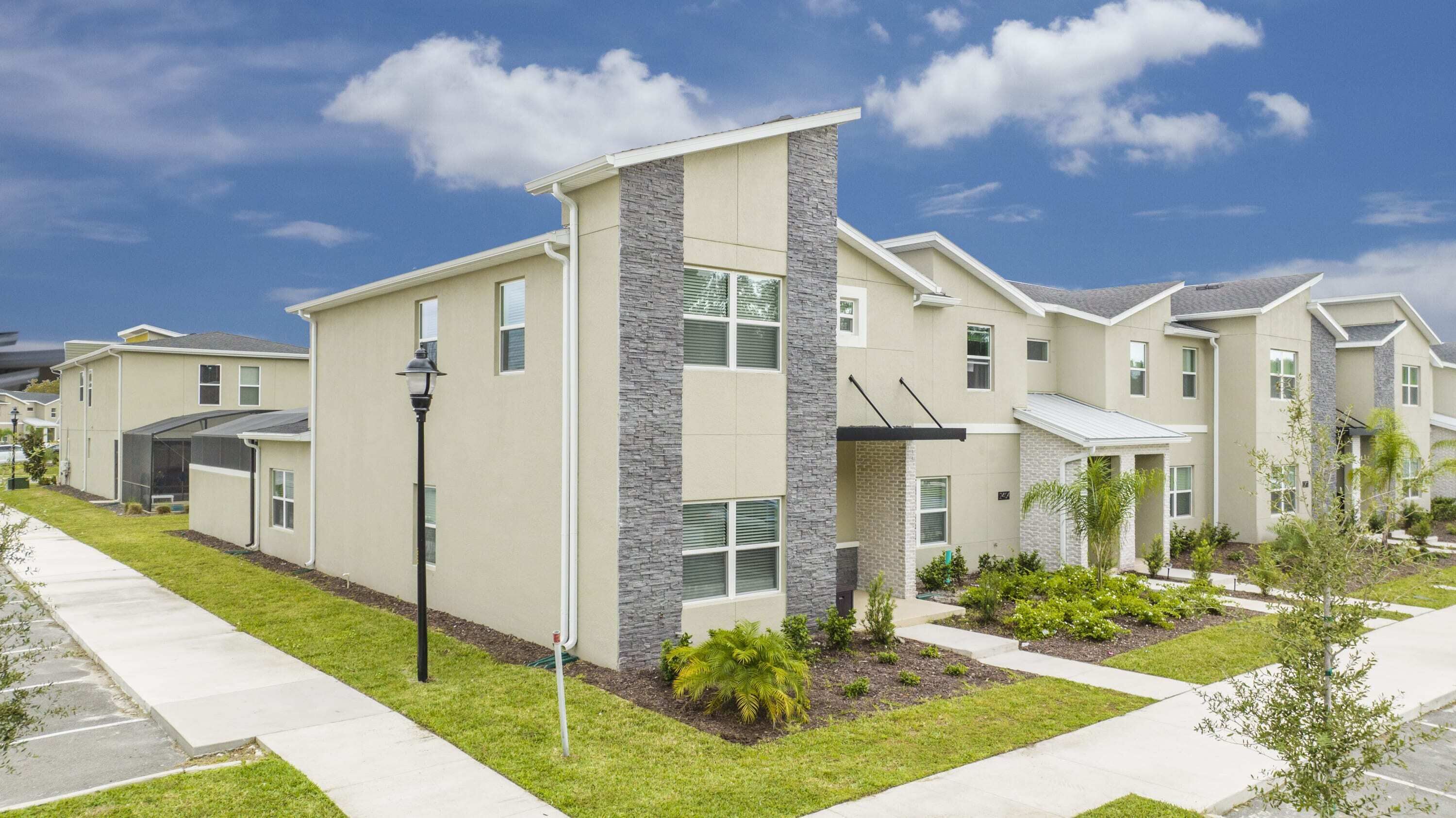 A modern residential building with a central tower, multiple windows, and a well-maintained lawn.