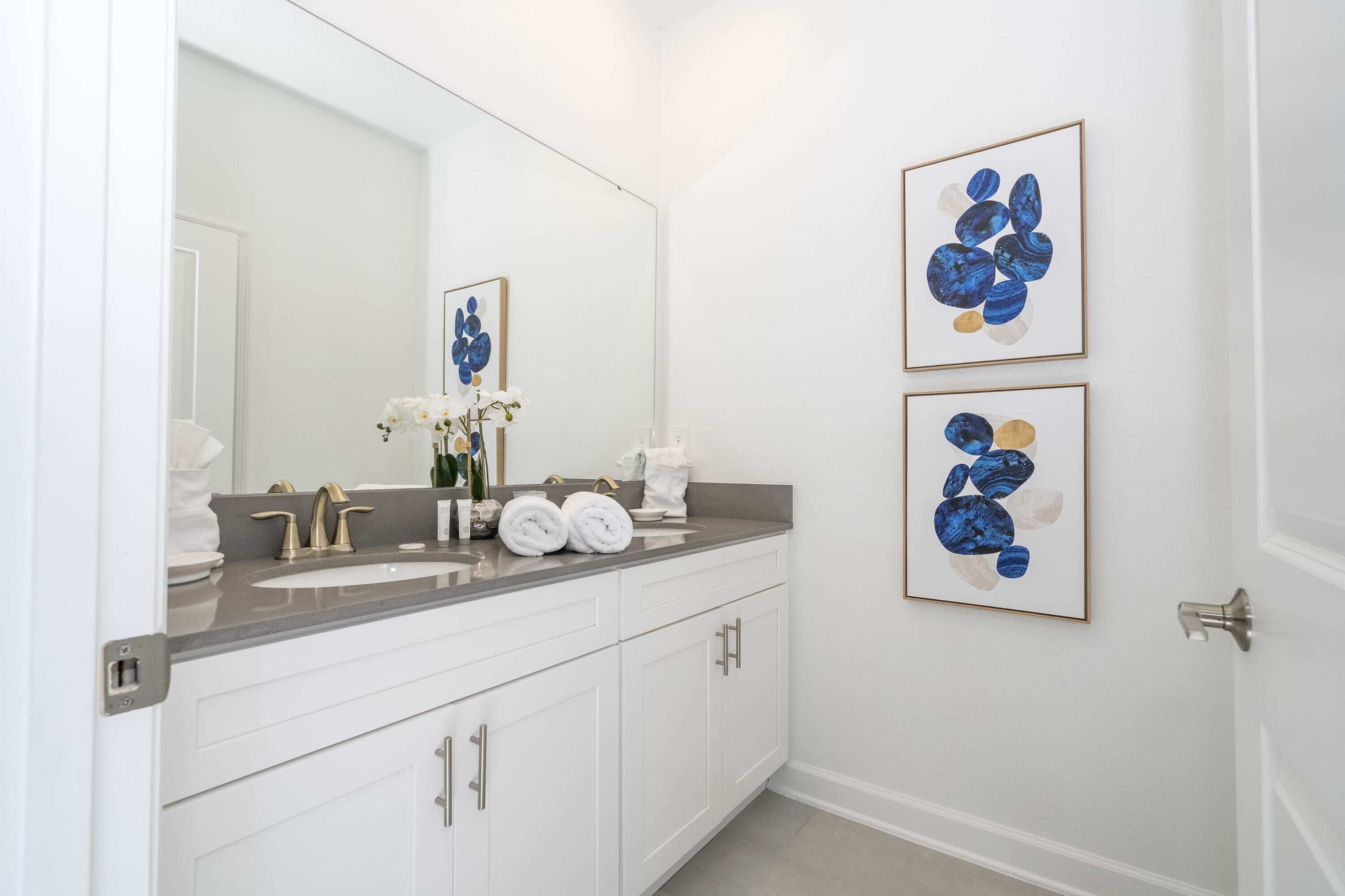 A bathroom with a white vanity, a large mirror, and two framed abstract art pieces on the wall.
