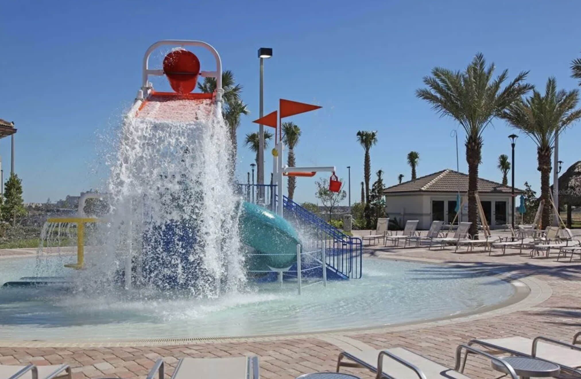 Un área de juegos acuáticos con un tobogán de agua grande, una piscina y sillas de descanso.