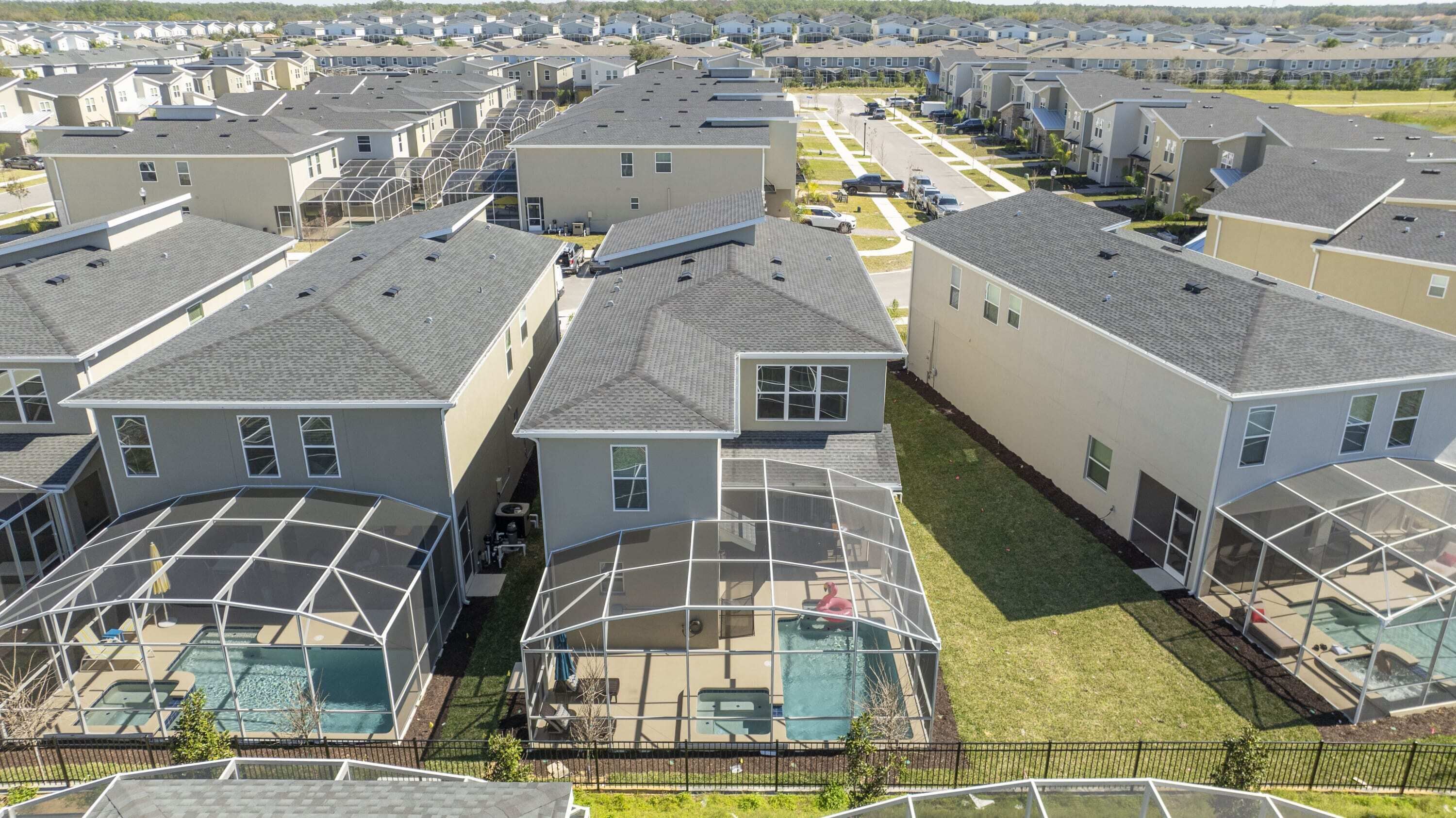 A residential area with multiple two-story houses, each featuring a covered outdoor swimming pool.