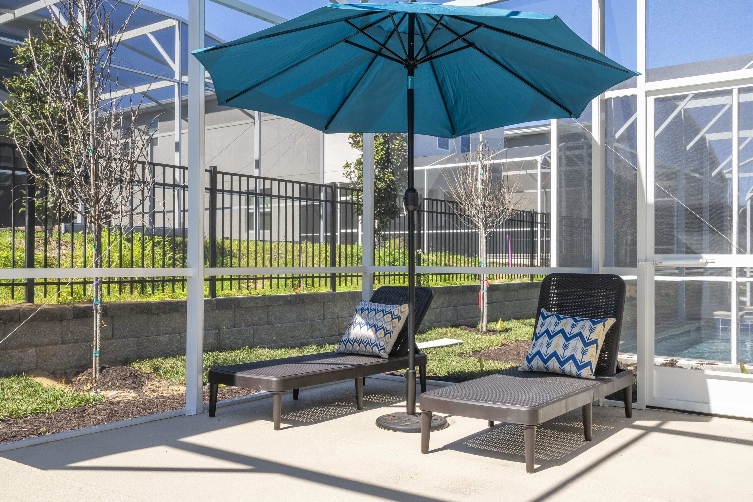 Een overdekt terras met twee loungestoelen en een blauwe parasol.