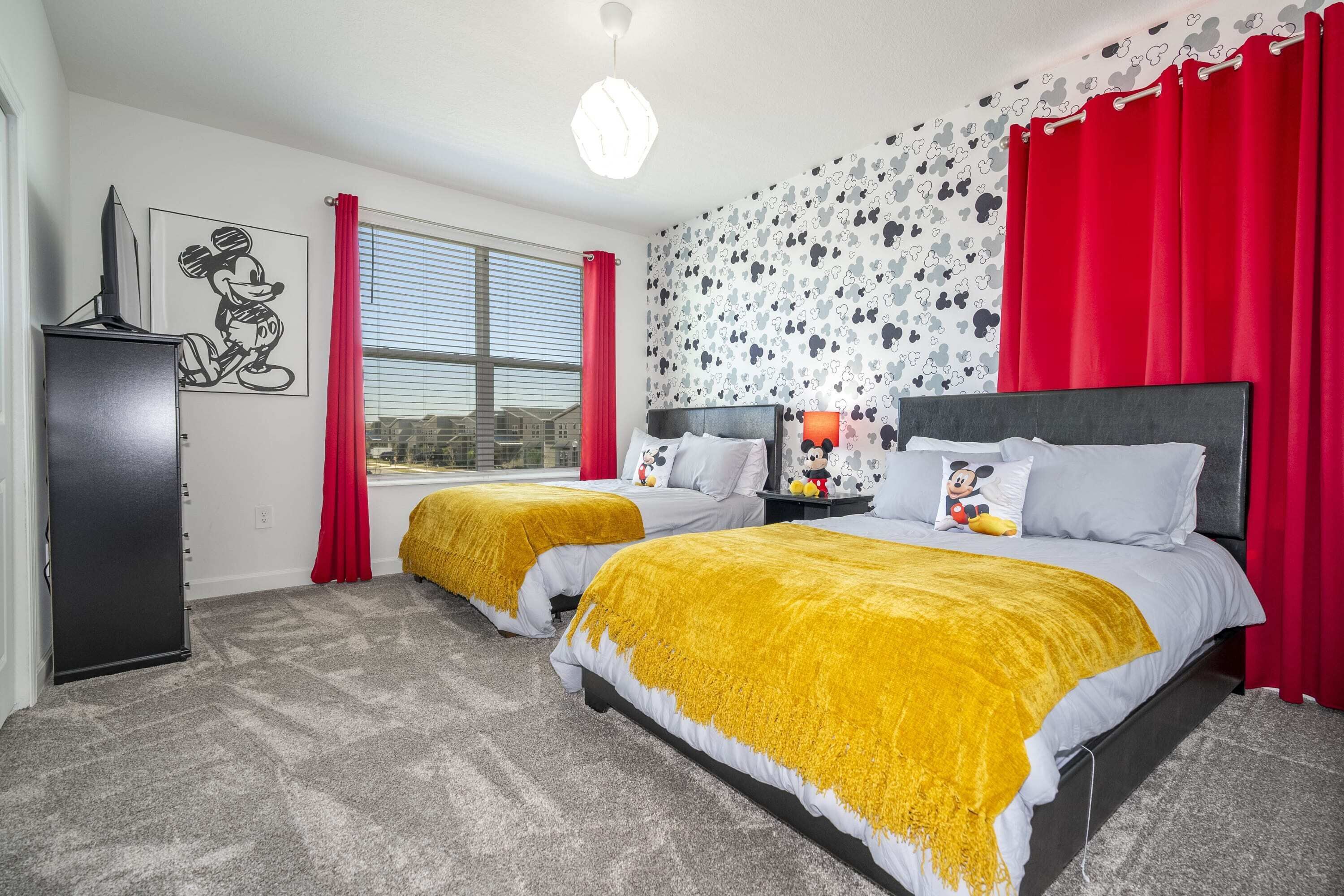 Een hotelkamer met twee bedden, een groot raam, een poster van Mickey Mouse en een Mickey Mouse-kussen.