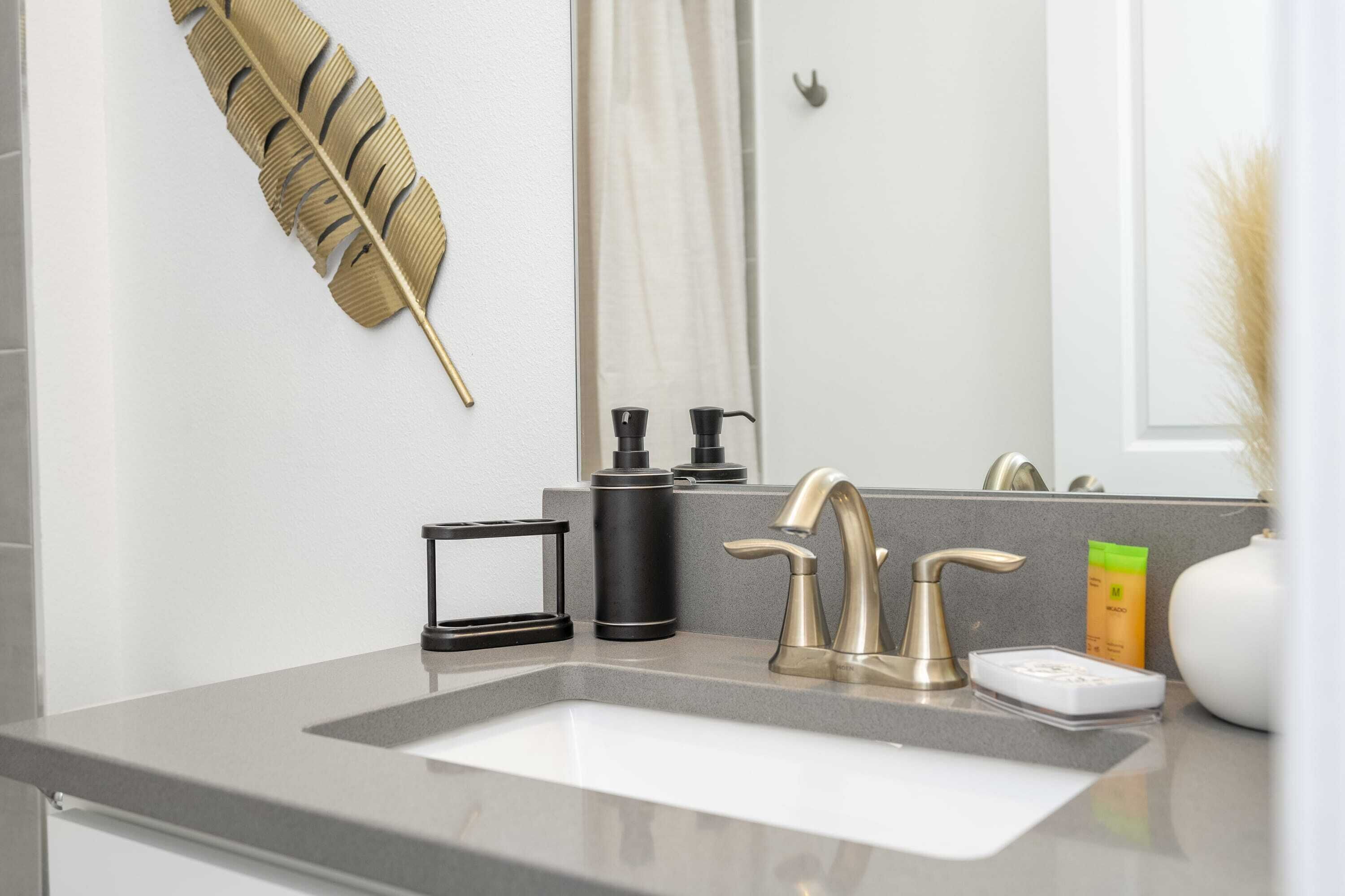 Un baño moderno con un espejo grande, una decoración de pluma dorada, un grifo y artículos de aseo en la encimera.