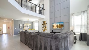 A spacious living area with a large gray sectional sofa, a staircase, and a flat-screen TV mounted on the wall.