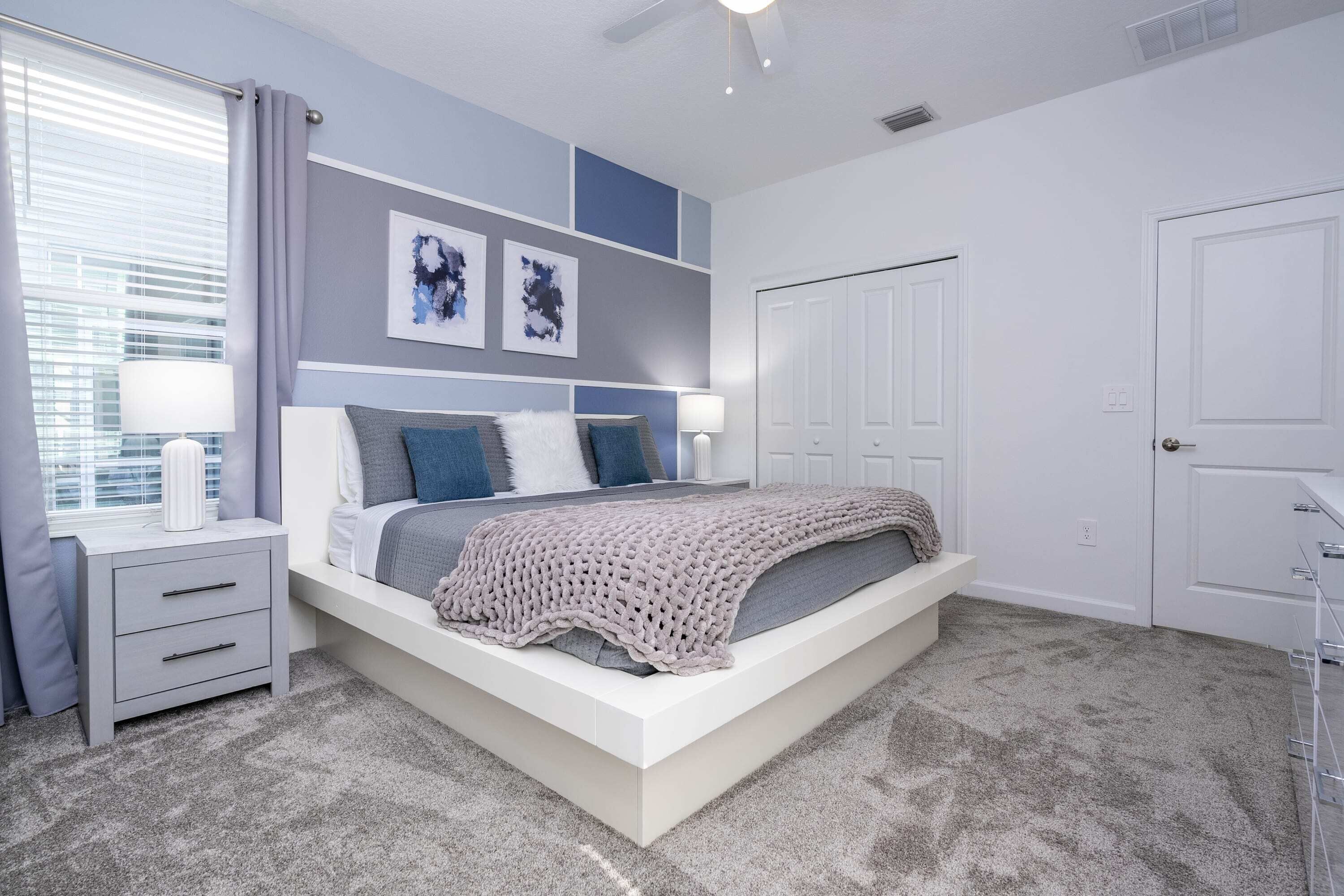 Un dormitorio con cama, mesitas de noche, una ventana con cortinas y una puerta.