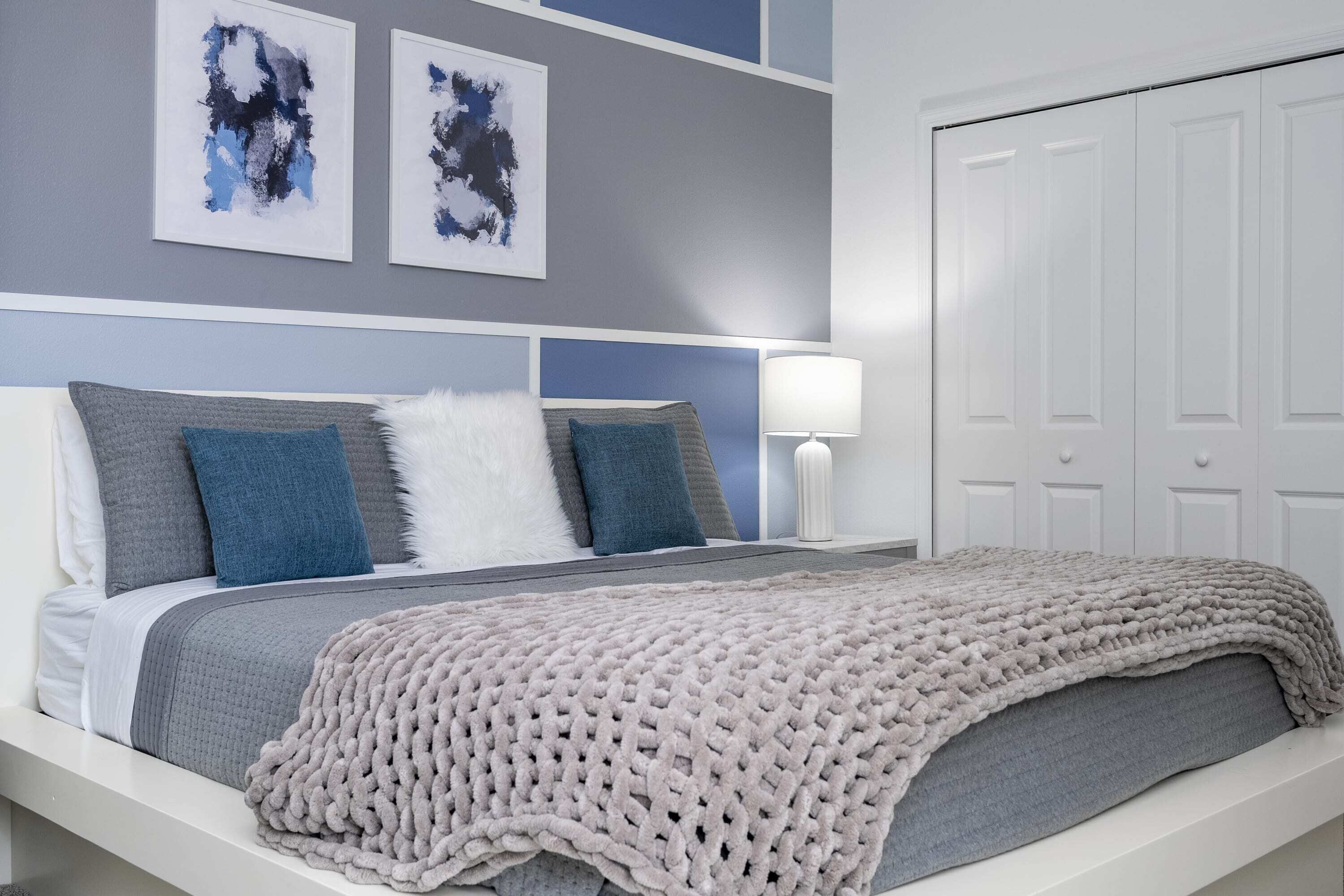 A neatly arranged bedroom with a bed, pillows, a blanket, and a bedside lamp.