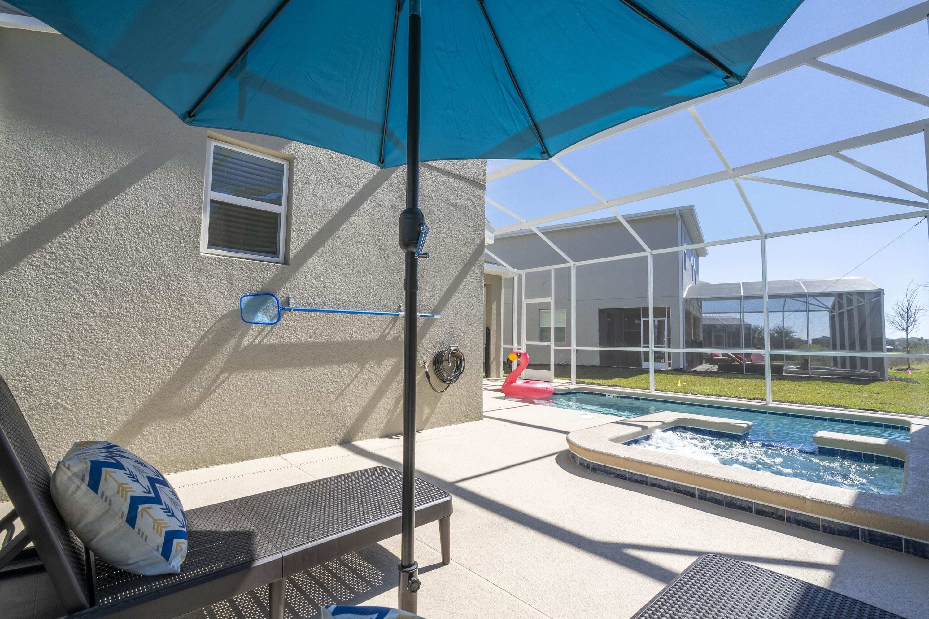 Uma área de piscina com hidromassagem, espreguiçadeiras e um guarda-sol azul.
