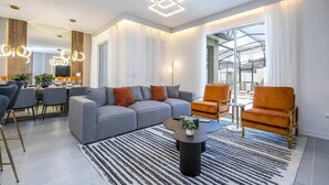 A modern living room with a grey sofa, orange armchairs, a coffee table, and a dining area with a glass top table. - Wonderful 4Bd | Pool |Close To Disney | 2669 (Kissimmee)