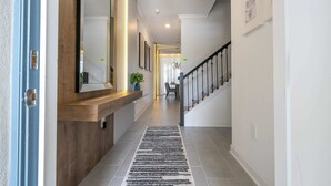 A hallway with a wooden bench, a black and white rug, and a staircase with a black railing. - Wonderful 4Bd | Pool |Close To Disney | 2669 (Kissimmee)
