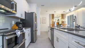 A modern kitchen with stainless steel appliances, white cabinetry, and a central island with seating. - Wonderful 4Bd | Pool |Close To Disney | 2669 (Kissimmee)