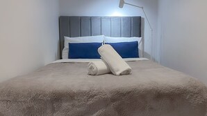 A neatly made bed with a grey headboard, a white and blue pillow, and a rolled white towel. - Skytower Escape:Modern 2B Apt (Brisbane City)