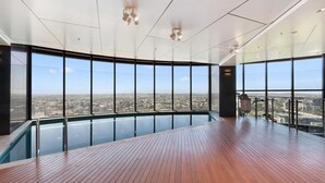 A modern indoor swimming pool with a wooden deck and large windows offering a city view. - Skytower Escape:Modern 2B Apt (Brisbane City)
