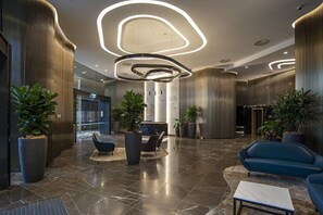 A modern lobby with a marble floor, seating areas, and large potted plants.