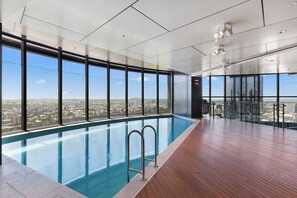 Une piscine intérieure moderne, dotée de grandes fenêtres et offrant une vue sur la ville.