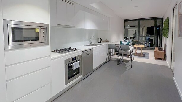 A modern kitchen with white cabinetry, stainless steel appliances, and a dining area with a round table and bar stools. - Skytower Escape:Modern 2B Apt (Brisbane City)