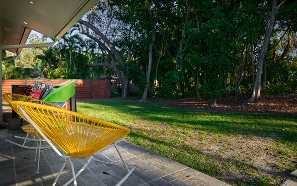 A patio area with a yellow wicker chair, a green umbrella, and a red bag on a tiled floor.