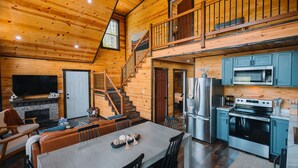 Una cabaña espaciosa con comedor, cocina y una escalera que sube a un altillo.
