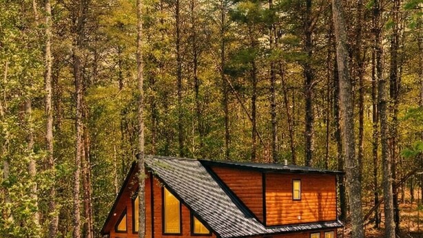 Una cabaña de madera con un balcón, rodeada de árboles.