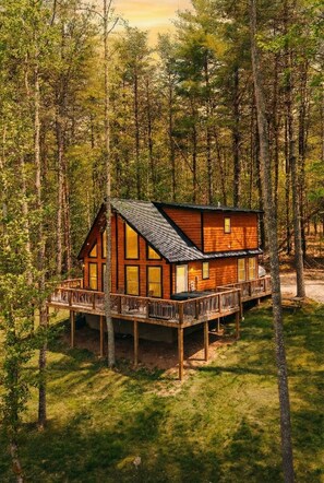 A wooden cabin with a deck, surrounded by trees.