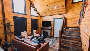 Un interior acogedor de cabaña con sala de estar, chimenea y escalera de madera.
