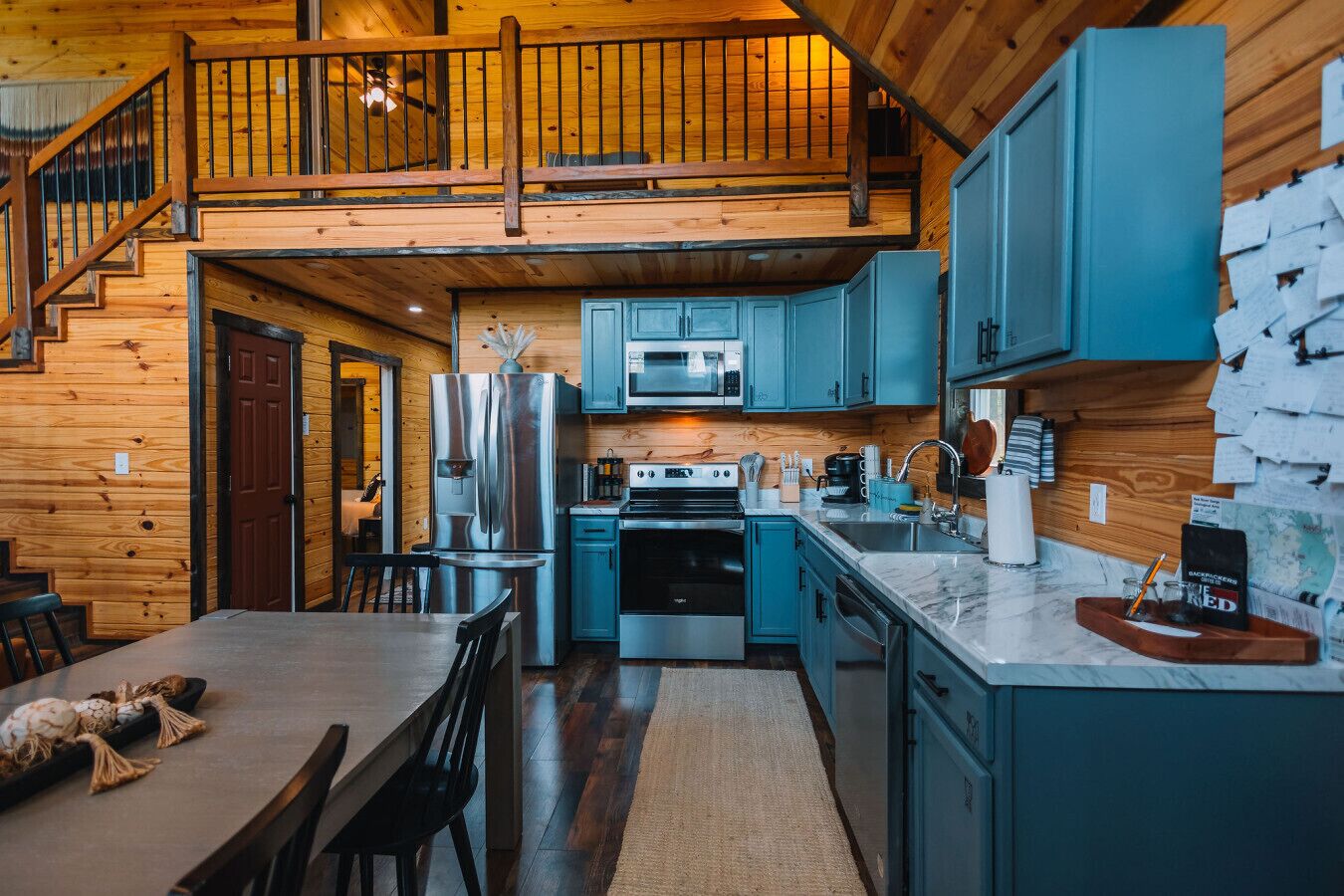 A modern kitchen with a central island, stainless steel appliances, and teal cabinetry.