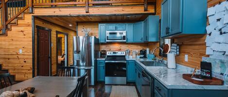 A modern kitchen with a central island, stainless steel appliances, and teal cabinetry.