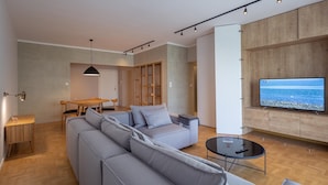A modern living room with a grey sofa, a coffee table, and a TV mounted on a wooden wall. - Hippocrates - Faliro Deluxe Apartment (Palaio Faliro)