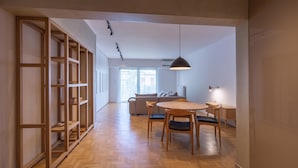 A modern interior with a wooden herringbone floor, a dining area with a round table and chairs, and a built-in bookshelf. - Hippocrates - Faliro Deluxe Apartment (Palaio Faliro)