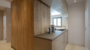 A modern kitchen with a wooden accent wall, a coffee maker, and a sink. - Hippocrates - Faliro Deluxe Apartment (Palaio Faliro)