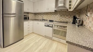 A modern kitchen with stainless steel appliances, white cabinetry, and a checkered backsplash. - Cassiopeia - Glyfada Apartment (Glyfada)