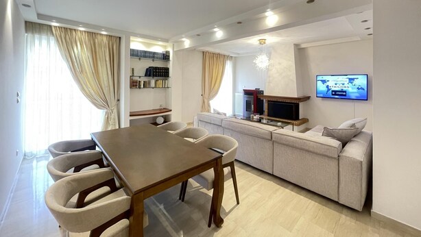 A modern living room with a dining area, a sofa set, a TV mounted on the wall, and a fireplace. - Cassiopeia - Glyfada Apartment (Glyfada)