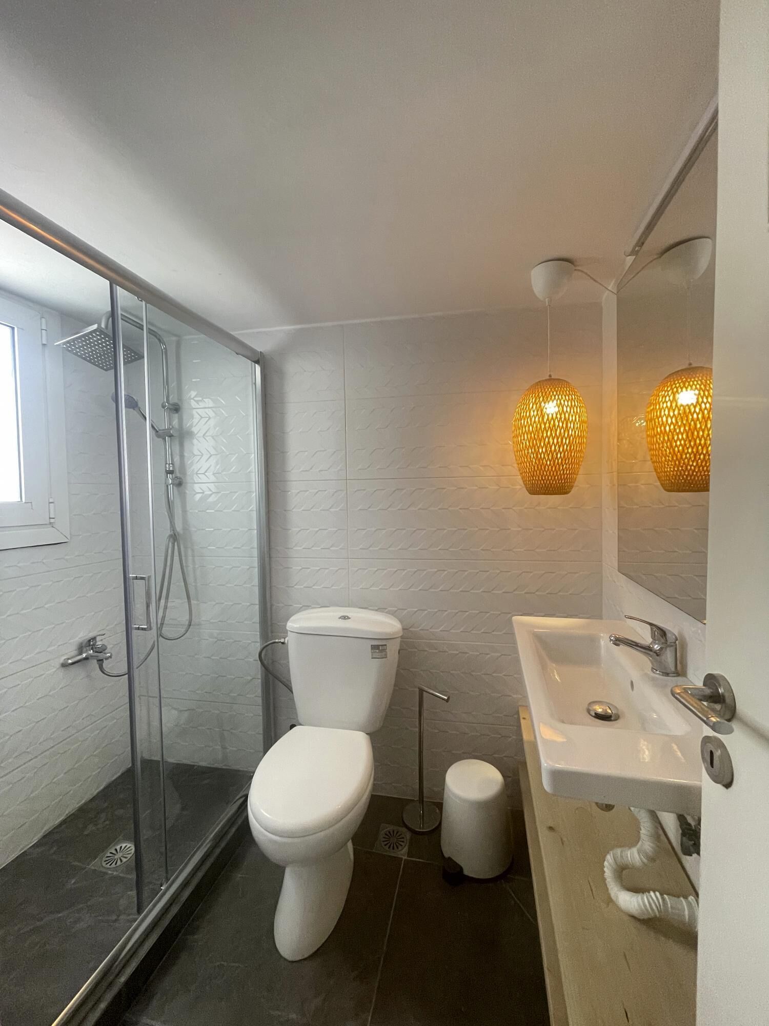 Uma casa de banho moderna com chuveiro envidraçado, sanita branca e lavatório com espelho.