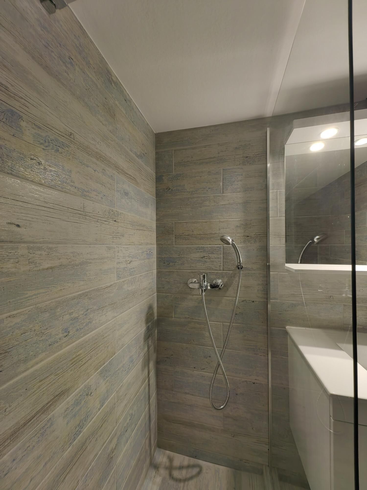 A modern bathroom with wooden panel walls, a glass shower enclosure, and a white sink.