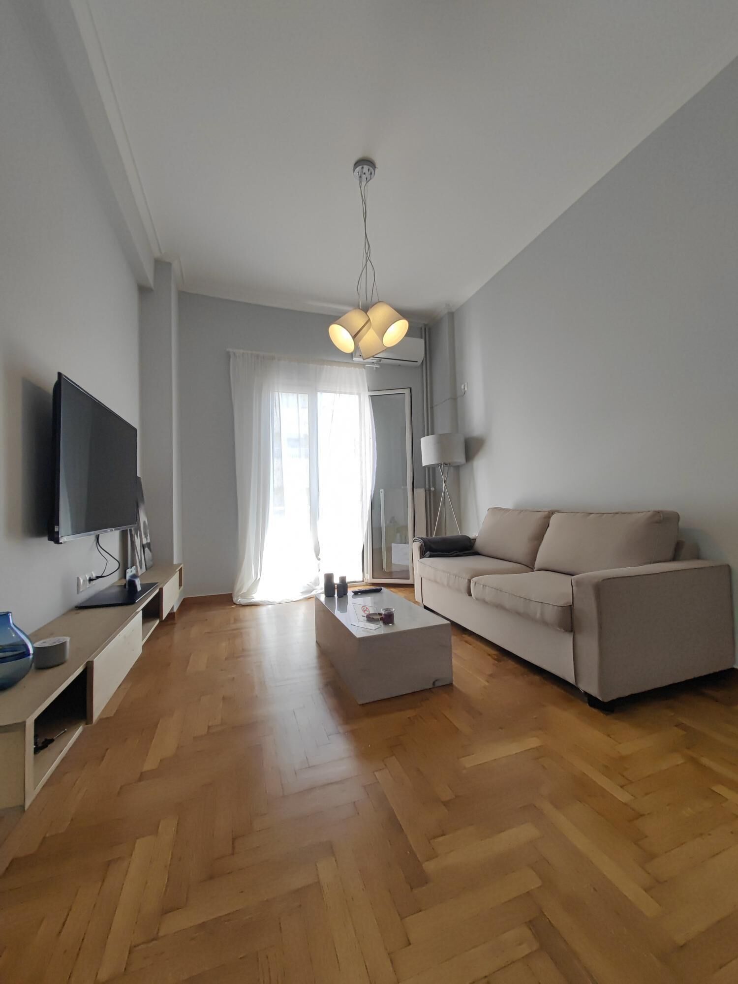 A modern living room with a flat-screen TV, a sofa, a coffee table, and a lamp.