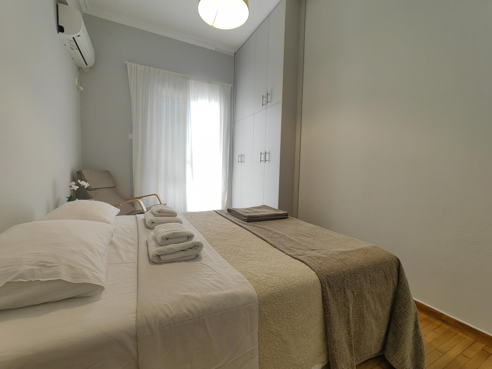 A hotel room with two beds, a wardrobe, a bedside table, and a window with curtains.