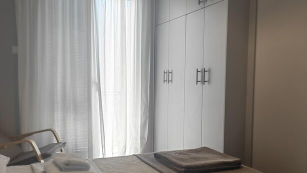 Una habitación de hotel con cama, mesita de noche, armario y ventana con cortinas.