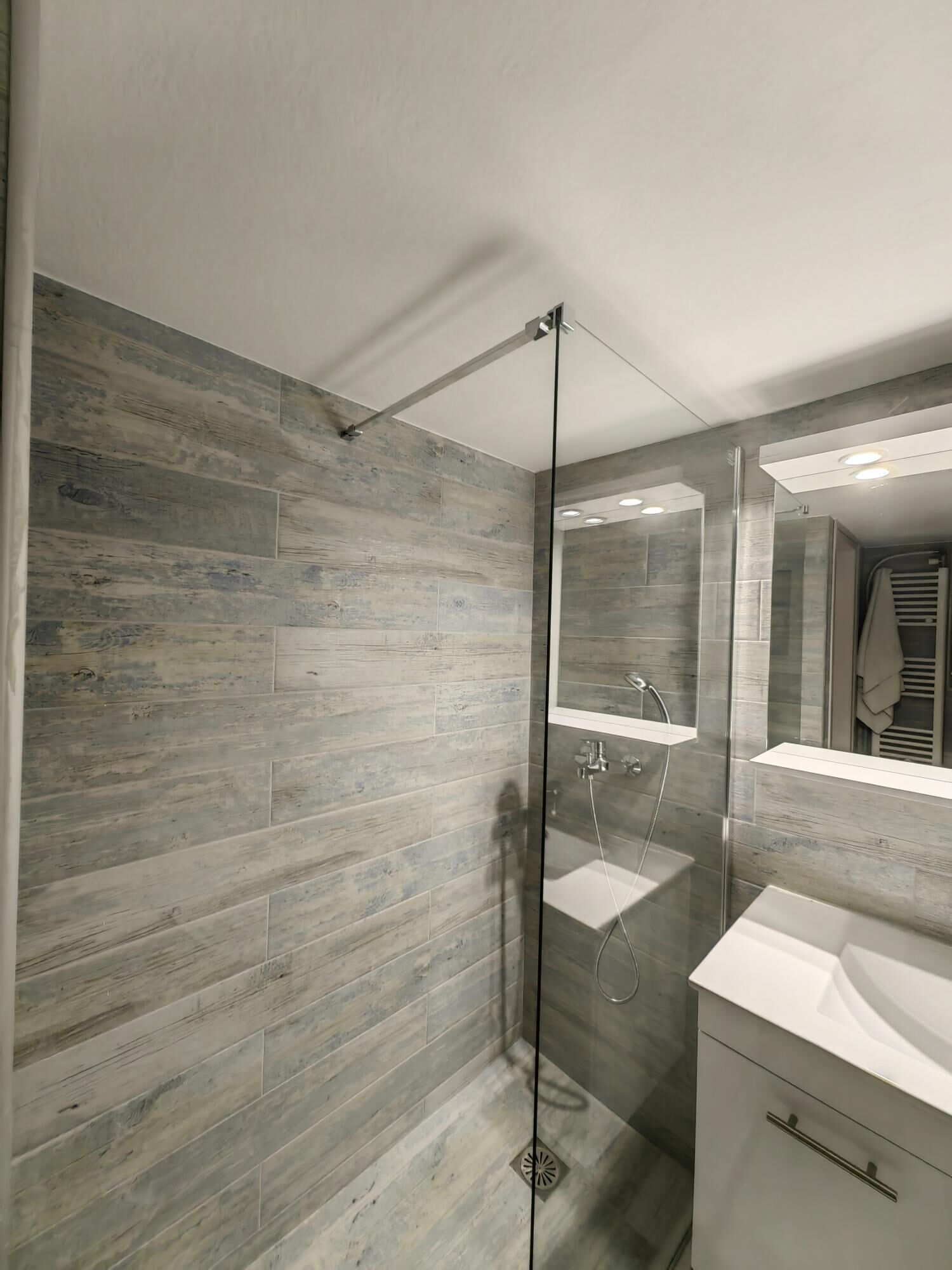 Un baño moderno con ducha acristalada, un espejo grande y un tocador blanco.