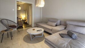 A modern living room with a sofa, a round coffee table, a chair, and a hanging light fixture. - Demetra - Koukaki Center Apartment (Athens)