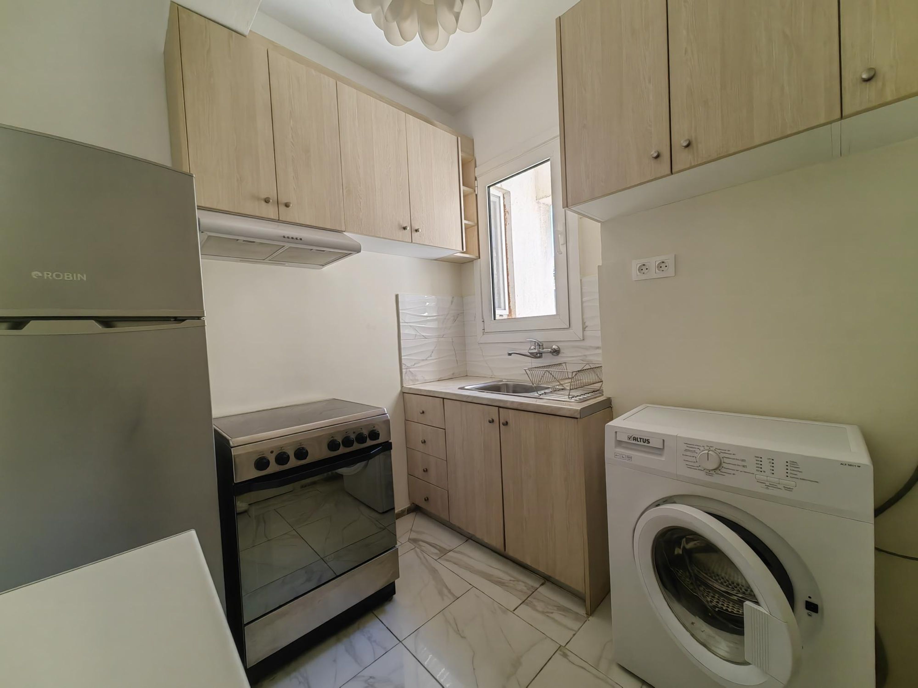 A compact kitchen with a built-in oven, a washing machine, and wooden cabinets.