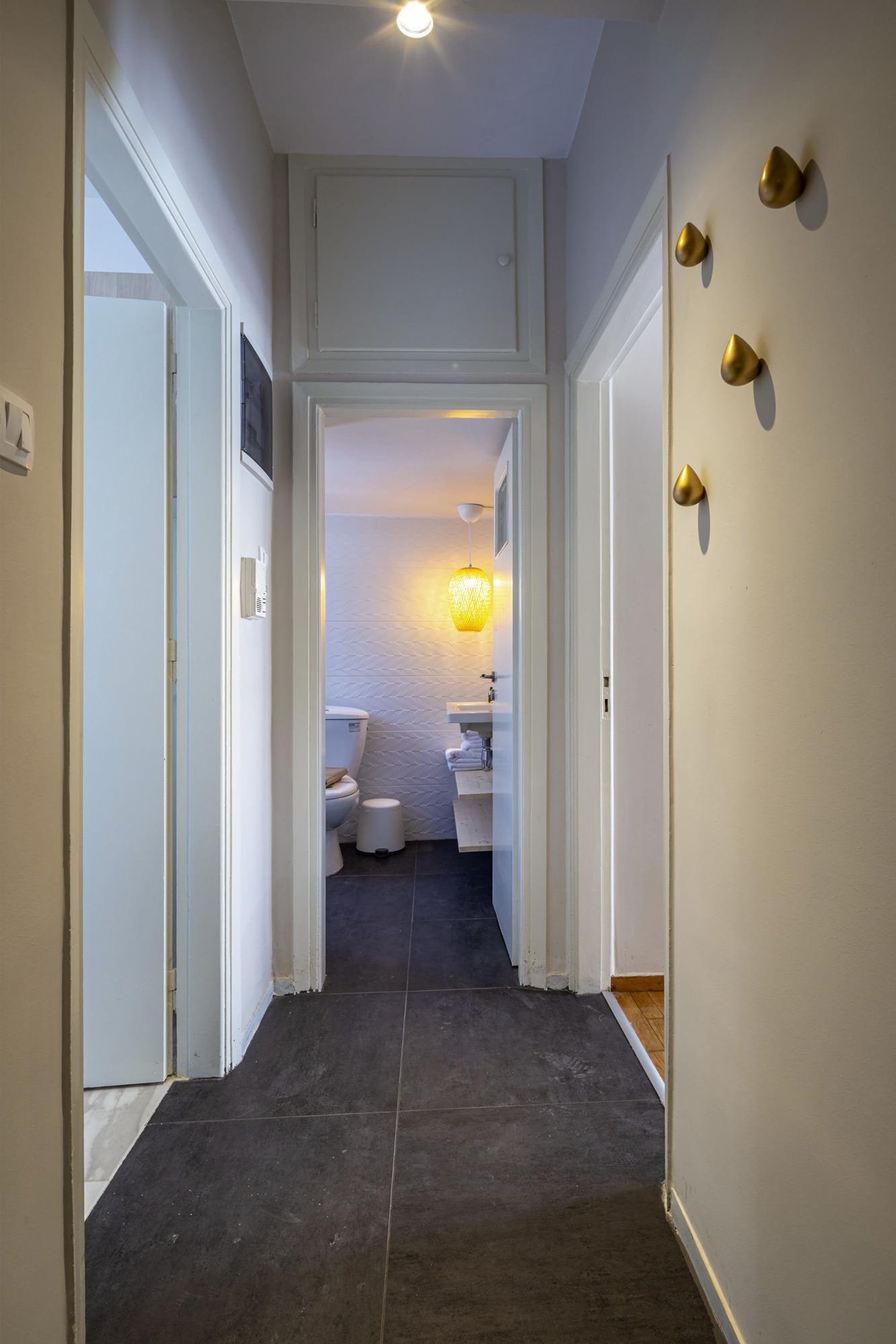 A narrow hallway leading to a bathroom with a toilet, sink, and towel rack.