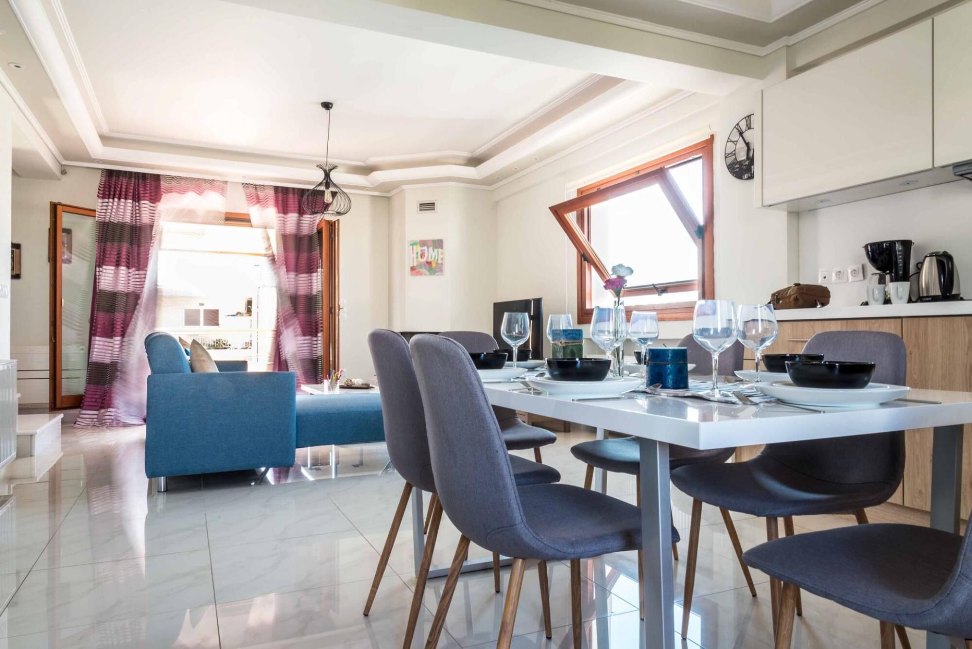 Un comedor moderno con una mesa blanca, sillas grises y un sofá azul al fondo.