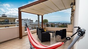 A balcony with a red hammock, black wicker furniture, and a view of the cityscape. - Leo - Unique Glyfada Apartment (Glyfada)