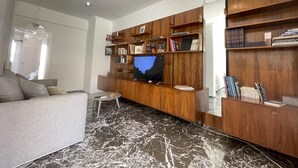 A modern living room with a flat-screen TV, wooden shelving, and a marble-patterned floor.