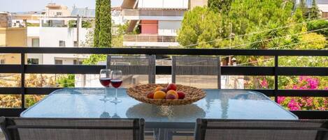 Ein Balkon mit einem Glastisch, zwei Stühlen, einer Korb mit Obst und zwei Weingläsern.