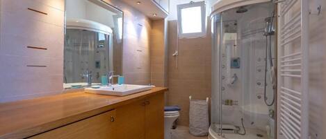 A modern bathroom with a wooden vanity, a large mirror, a glass-enclosed shower, and a small window.